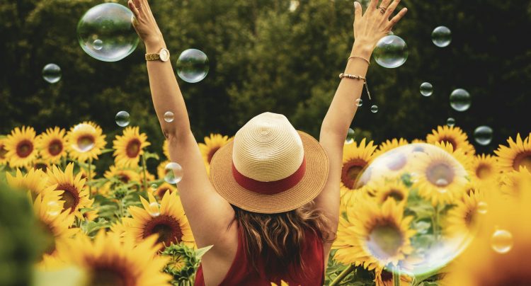 A joyful woman in a sunflower field with bubbles, expressing happiness on a summer day.