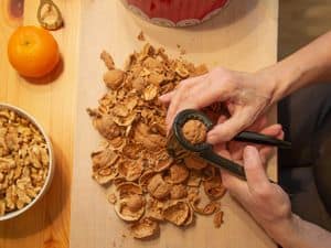 Close-up of hands cracking walnuts with a bowl of shelled nuts and an orange on a wooden table.