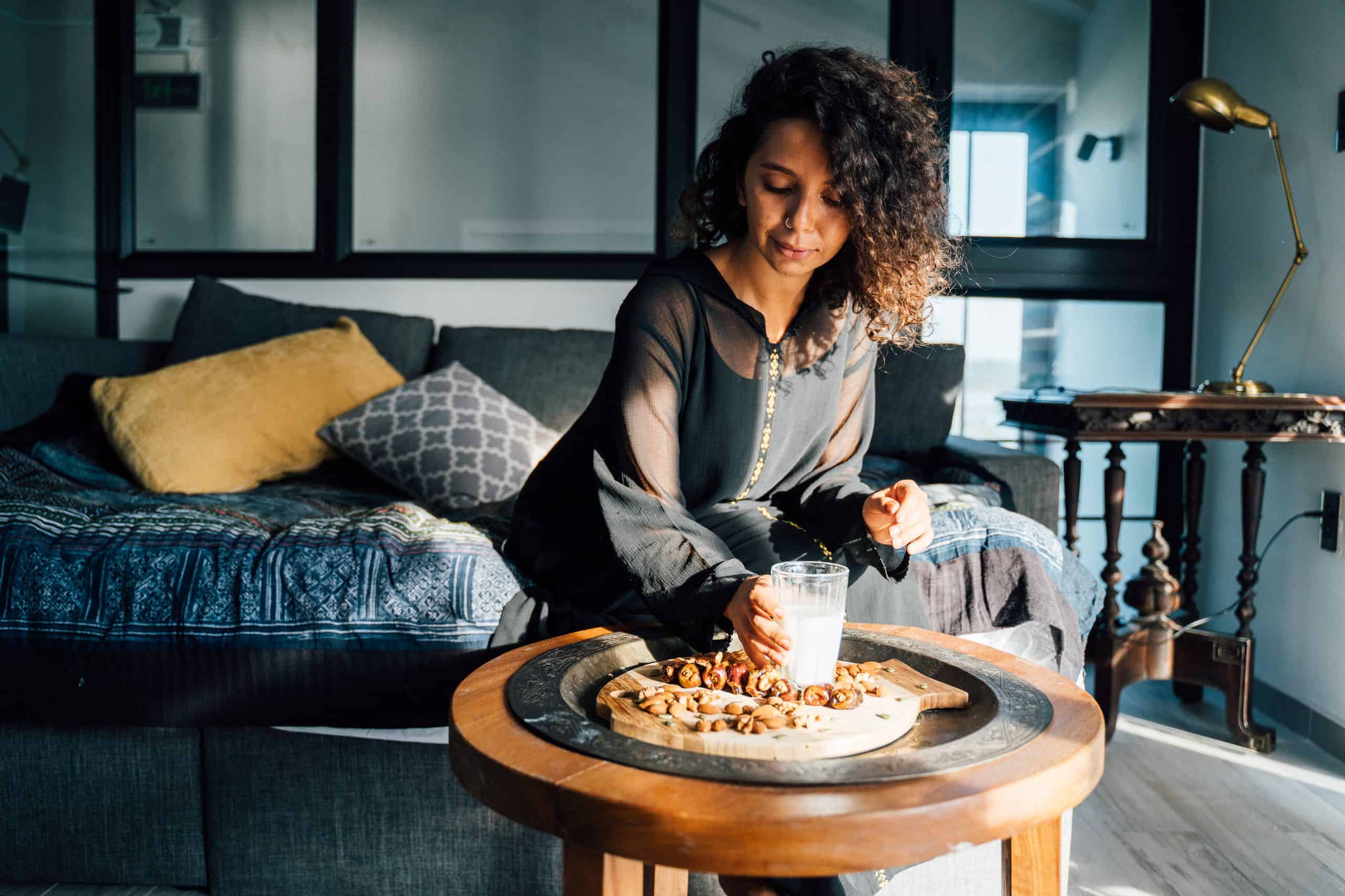 Woman in cozy living room enjoying snacks with a glass of milk on a sunny day.