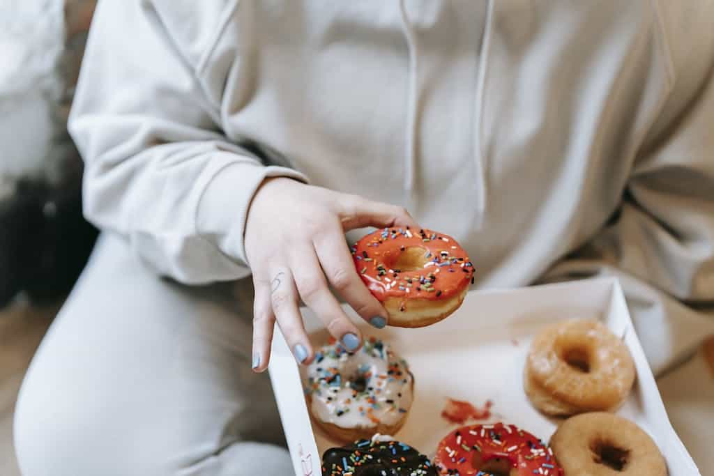 Crop faceless woman taking appetizing donut from box